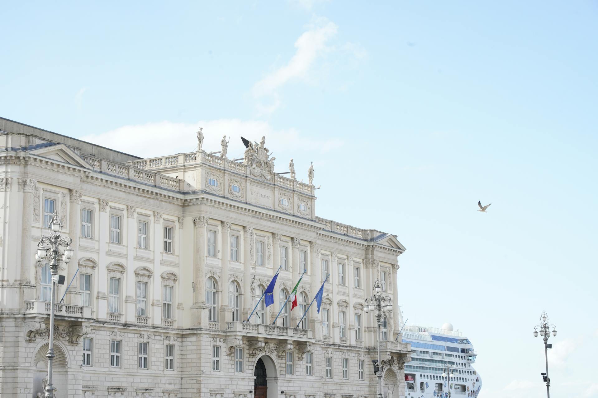 Historic Palazzo del Lloyd Triestino with flags in Trieste, Italy, under a clear sky, highlighting its architectural beauty.