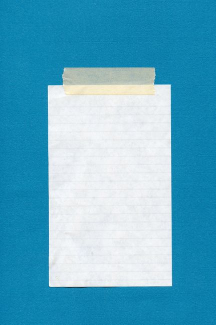 Vertical shot of a blank notebook page taped to a blue wall, ideal for copy space.