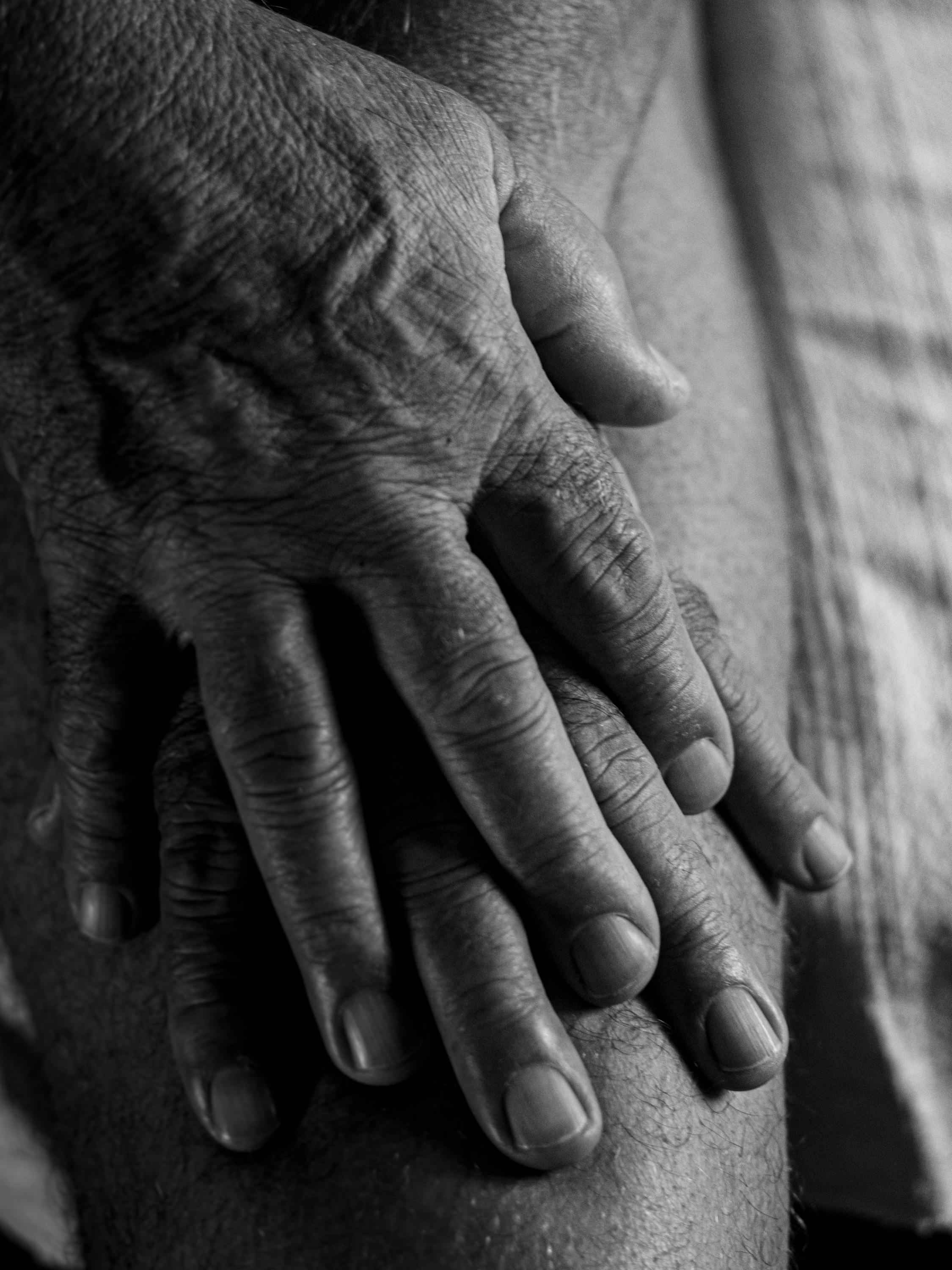 Black and white close-up of elderly man's hands pressing on his knee, showing detail and texture.