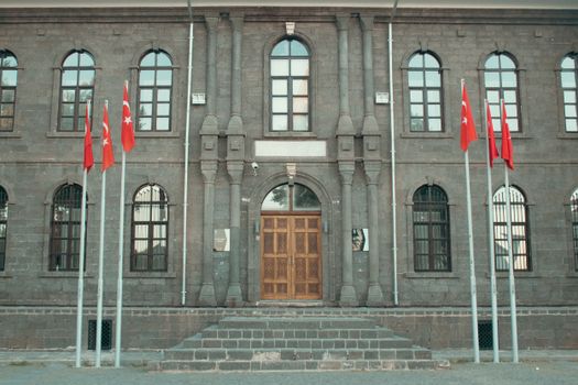 Front view of a historic stone museum with Turkish flags in Diyarbakır, Turkey.