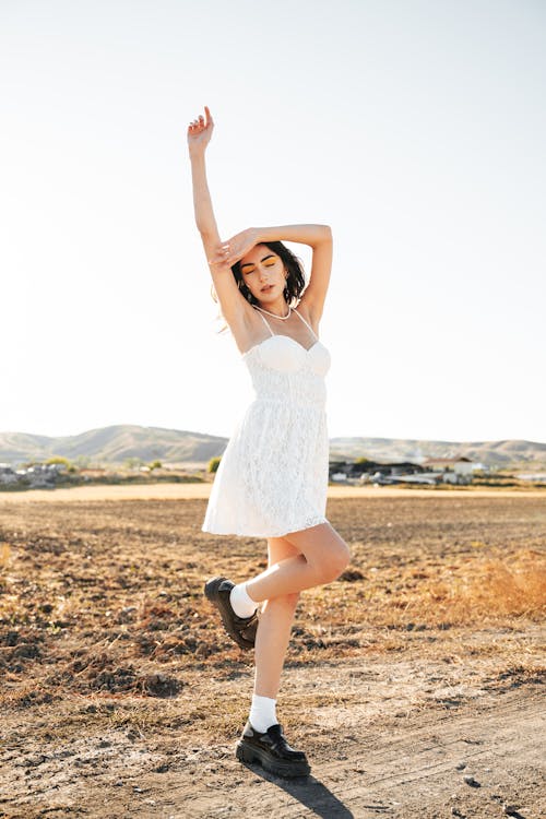 Model Wearing a White Spaghetti Strap Mini Dress Posing on a Dirt Road