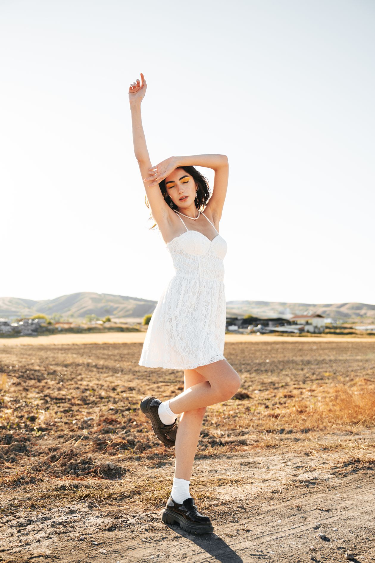Woman in a white lace mini dress posing in a field at golden hour