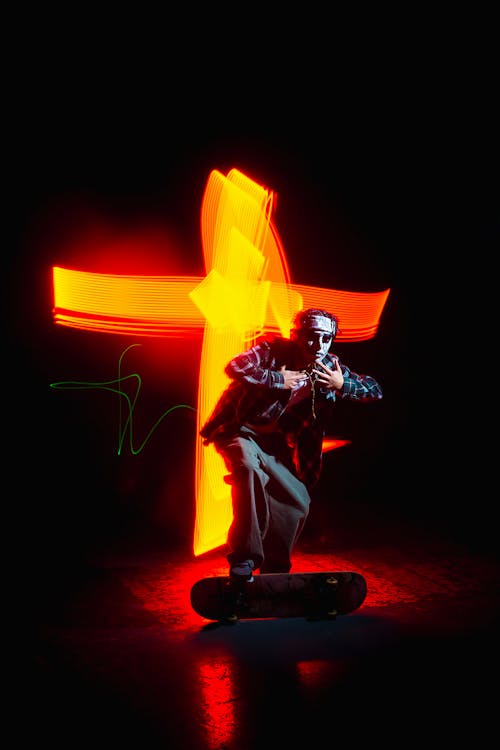 A Man with a Skateboard Standing on the Background of Bright Blurred Lights 