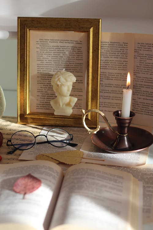 Lit Candle in a Candle Holder and a Decorative Candle Among the Pages From a Book