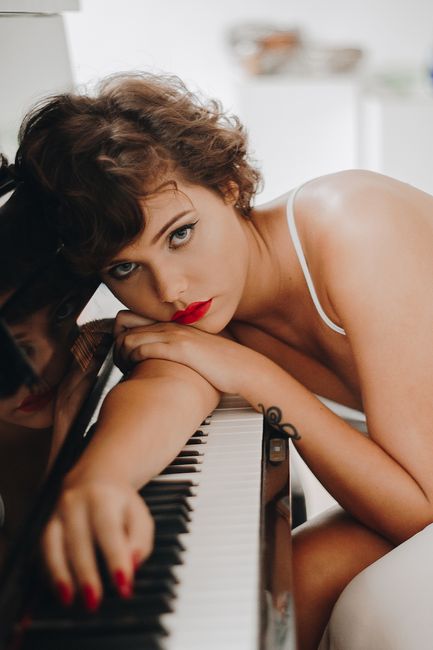 Elegant woman with striking red lipstick posing by a piano, showcasing beauty and style.