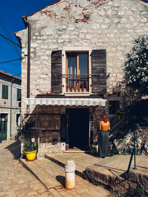 Free A woman stands before a rustic stone house in Rovinj's historic old town on a sunny day. Stock Photo