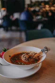 Close-up of gourmet lamb shank in spiced broth, shot indoors at a restaurant.