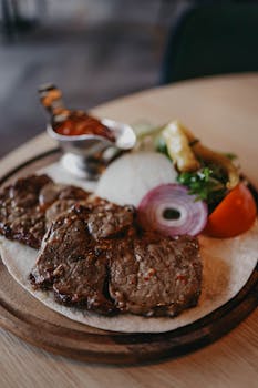 A savory grilled meat platter with fresh vegetables and dipping sauce on a rustic board.