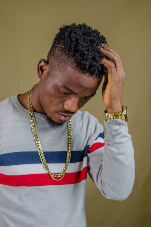 Young Man in a Casual Sweater and Gold Jewelry Fixing His Hair 