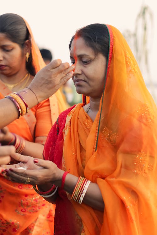 Women in Orange Sarees and Veils Standing Outside during a Traditional Ceremony 