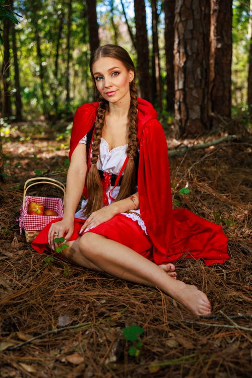 Free Woman in a Red Riding Hood costume sitting barefoot in a forest with a picnic basket. Stock Photo