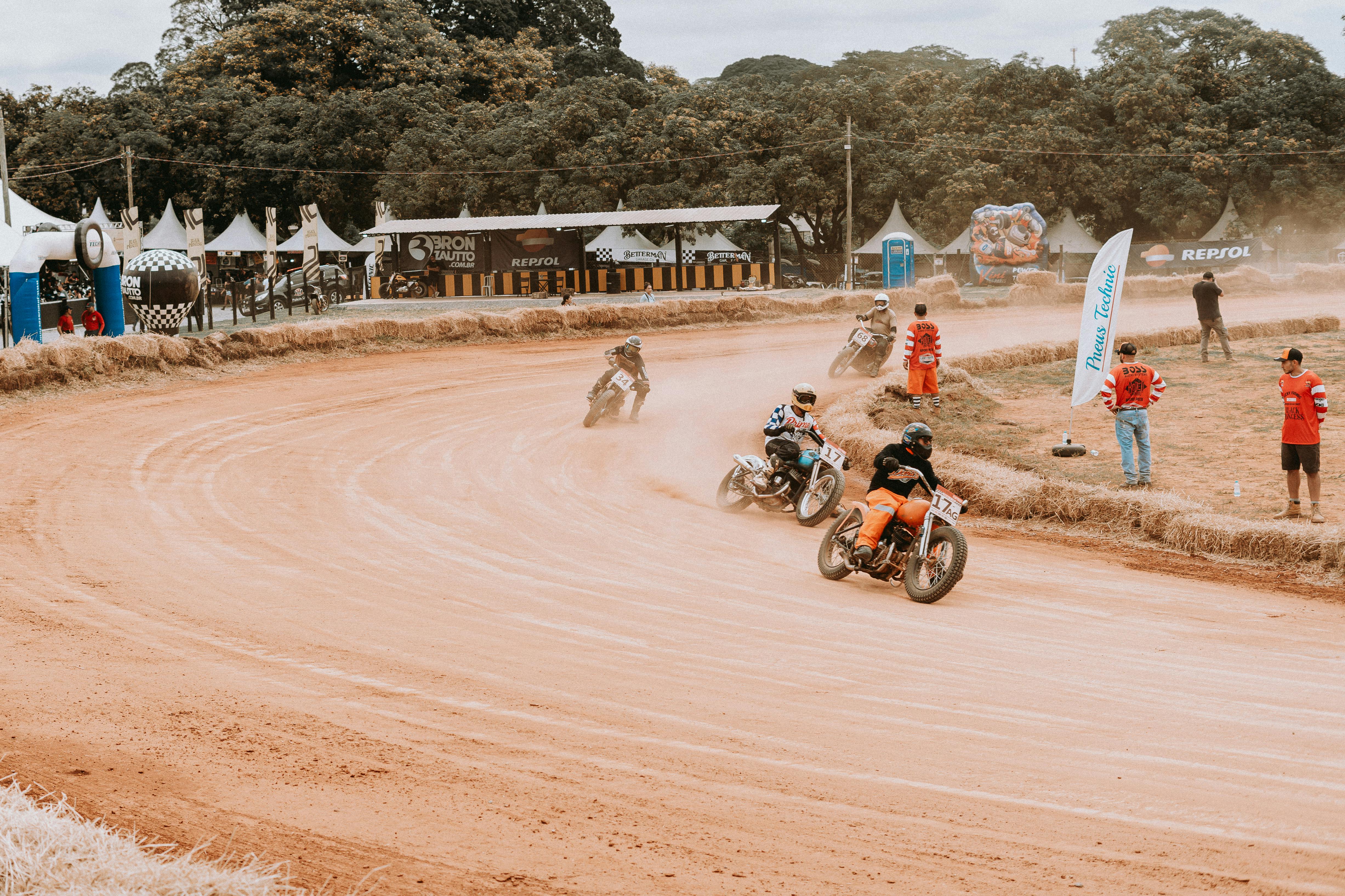 Motorcyclists racing on a dirt track at an outdoor sports event surrounded by spectators.