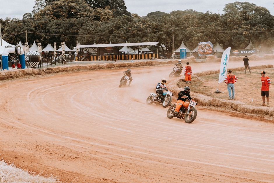 Motorcyclists racing on a dirt track at an outdoor sports event surrounded by spectators.