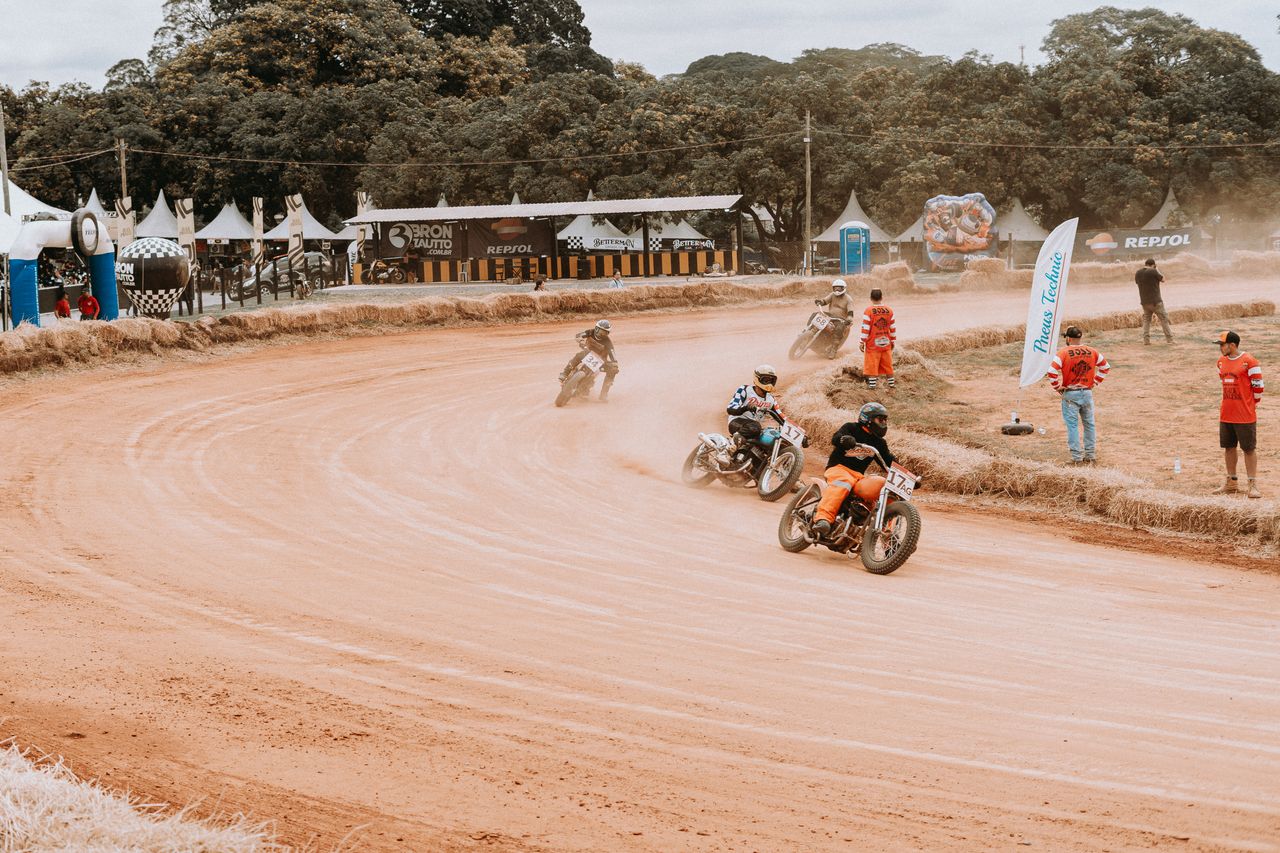 motorcyclists racing on a dirt track at an outdoor sports event surrou