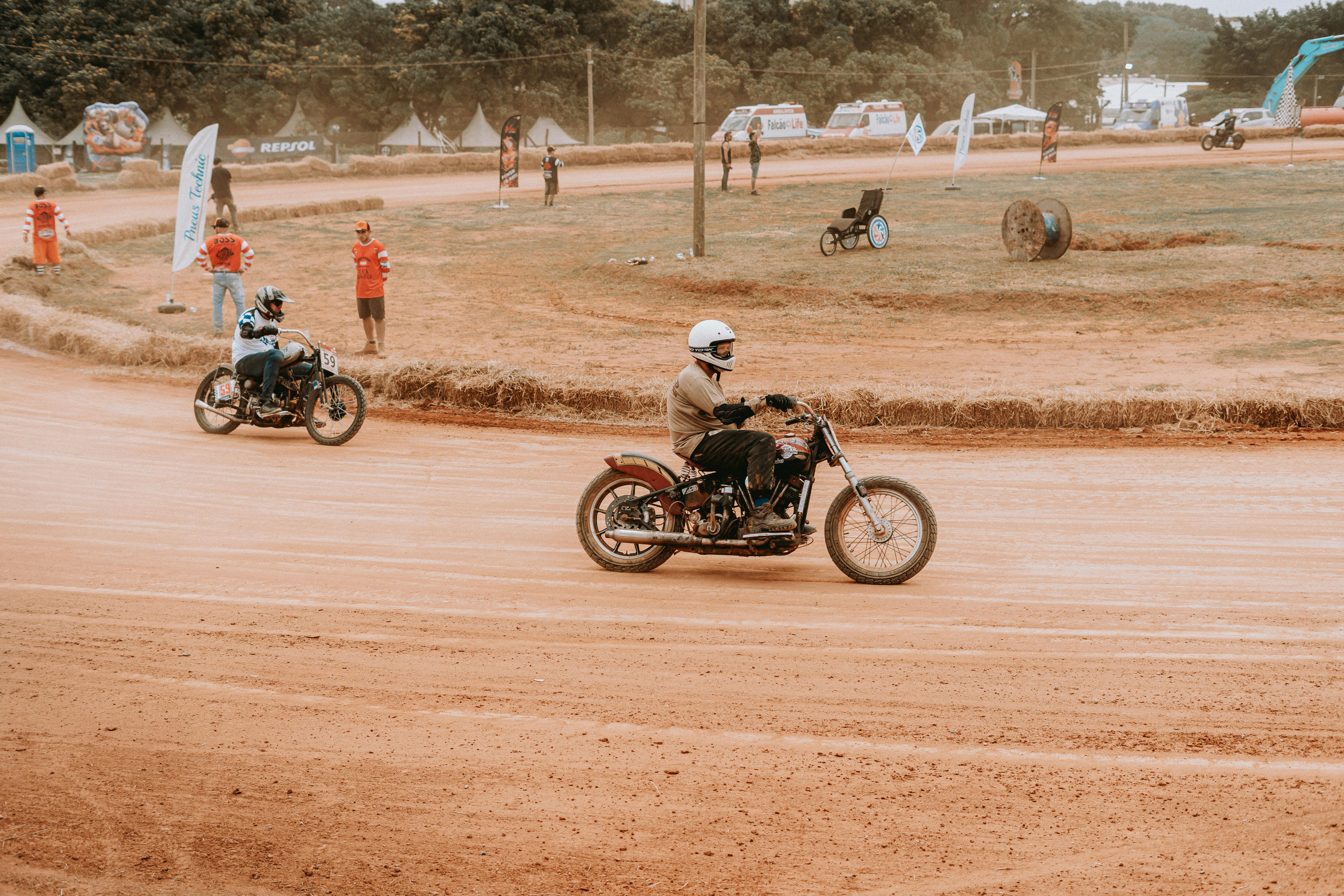 Motorcycles racing on a dusty outdoor track with spectators, showcasing speed and excitement.