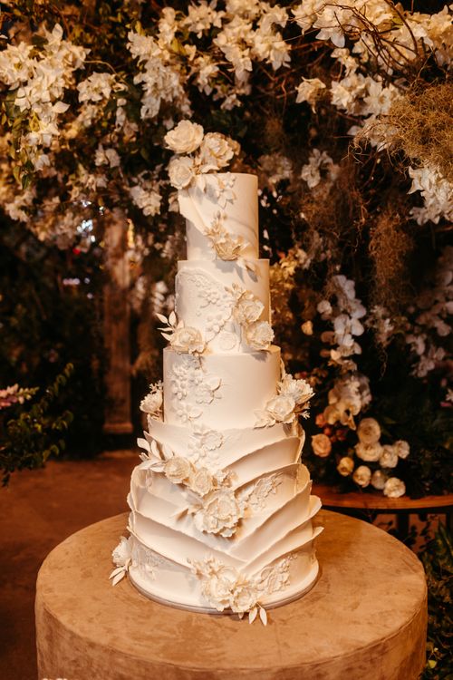 Free A sophisticated five-tier wedding cake adorned with white flowers against a floral backdrop, perfect for receptions. Stock Photo