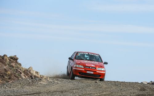 Free Red Fiat rally car kicking up dust on a rugged desert terrain during a race. Stock Photo