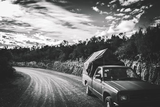 Black and white photo of a truck on a rural gravel road under a cloudy sky in San Bartolo, Mexico.