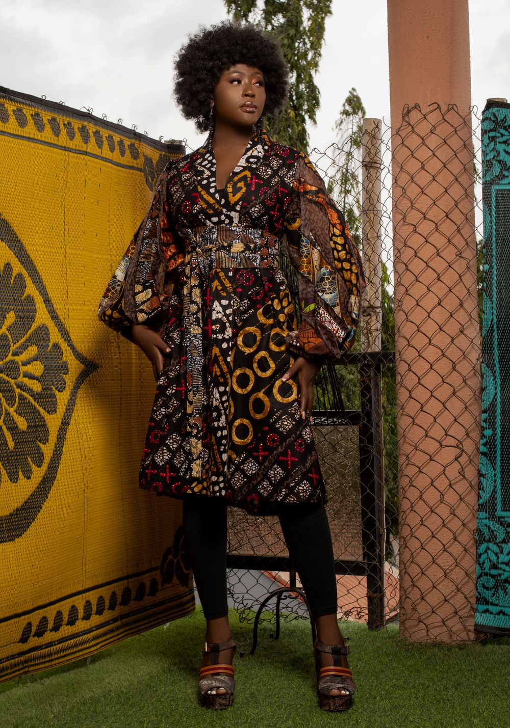Woman in a printed Ankara coat dress in front of a yellow wall