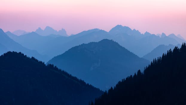 Breathtaking view of layered alpine mountains under a pastel sunset sky.