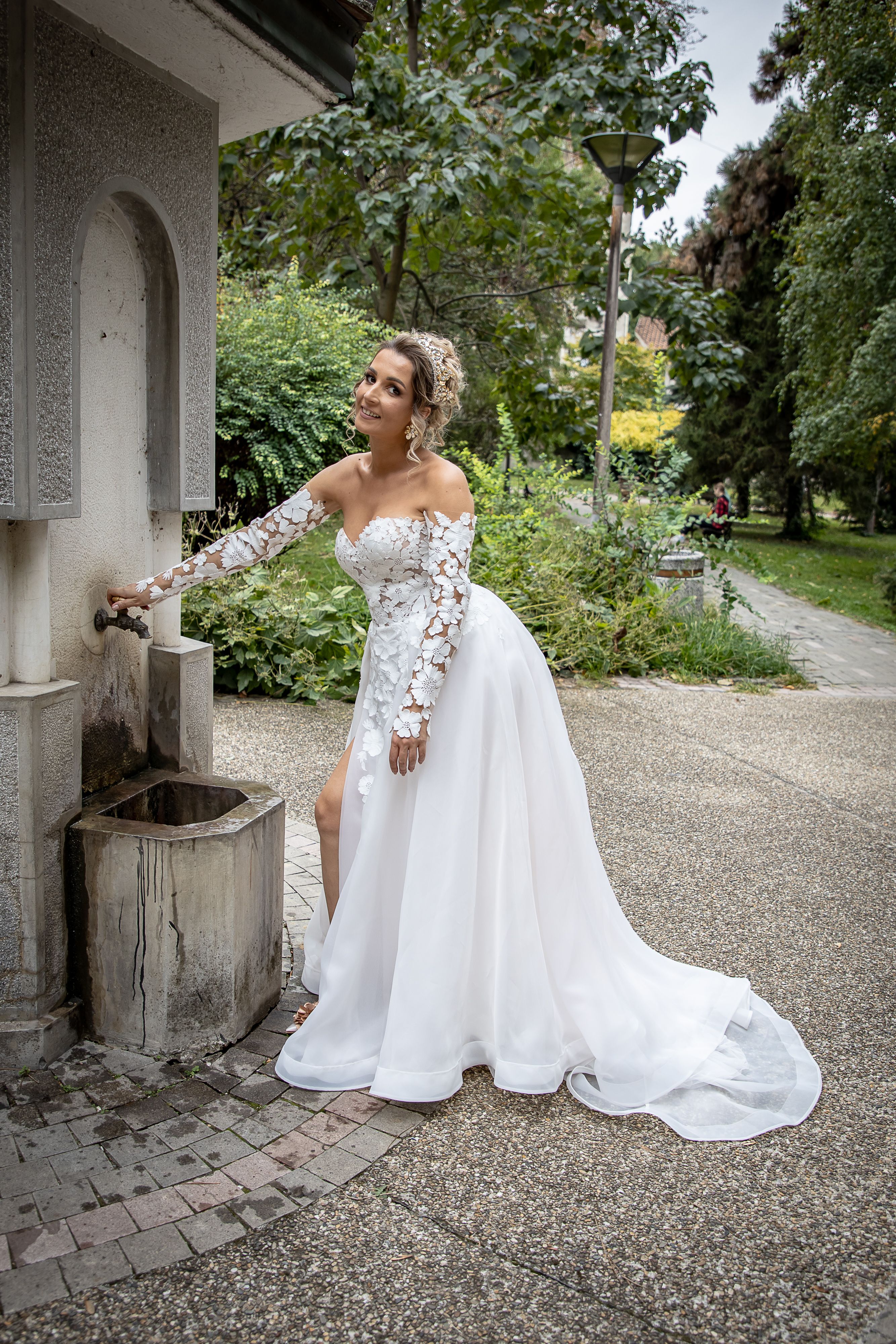 A smiling bride enjoying a refreshing moment at an outdoor fountain on her wedding day, dressed in a beautiful gown.
