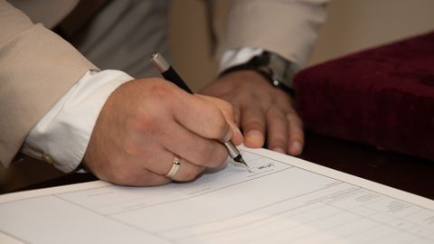 A close-up of a man signing a document, showcasing a wedding ring and pen.