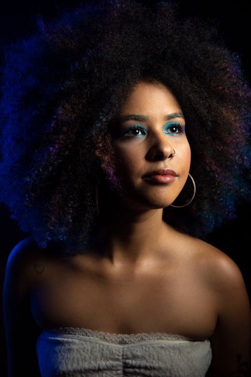 Free Intimate studio portrait of a young woman with afro hair and bold makeup, shot in dim lighting. Stock Photo