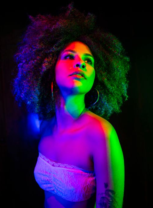 Free Colorful studio shot of a woman with afro hair illuminated by neon lights, expressing a lively nightlife vibe. Stock Photo