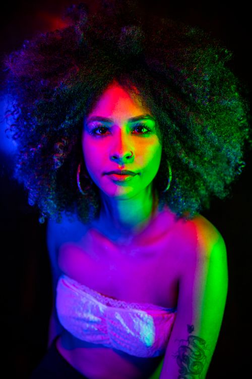 Free Colorful neon-lit portrait of a woman with afro hair in a white top, exuding a vibrant nightlife vibe. Stock Photo