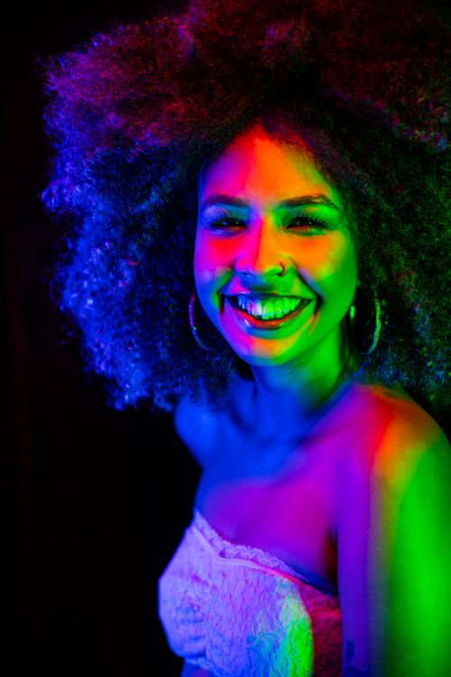 Free Cheerful woman with afro hair glowing under colorful neon lights in a studio. Stock Photo