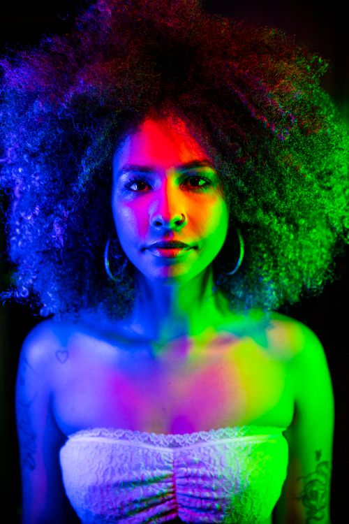 Free Colorful neon-lit portrait of a woman with curly afro hairstyle in studio setting. Stock Photo