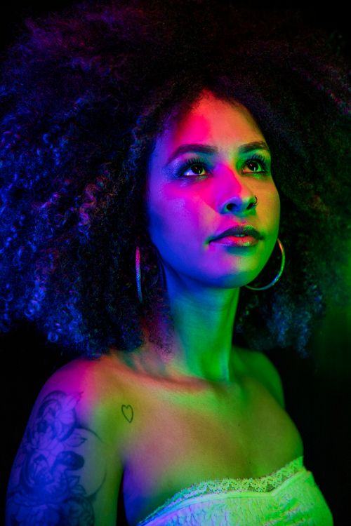 Free Vibrant studio portrait of a woman with curly afro hair and tattoos under colorful lighting. Stock Photo