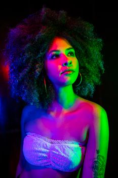 Vibrant portrait of a young woman with afro and tattoos under colorful lighting.
