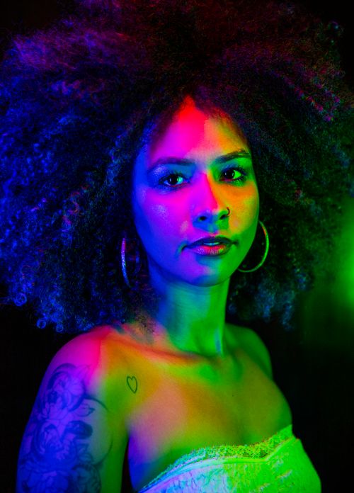 Free Colorful studio portrait of a woman with an afro and tattoos in vibrant lighting. Stock Photo