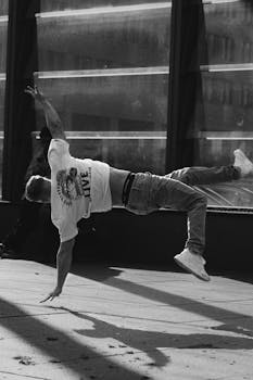 Black and white photo of a man breakdancing on an urban sidewalk, showcasing movement and creativity.