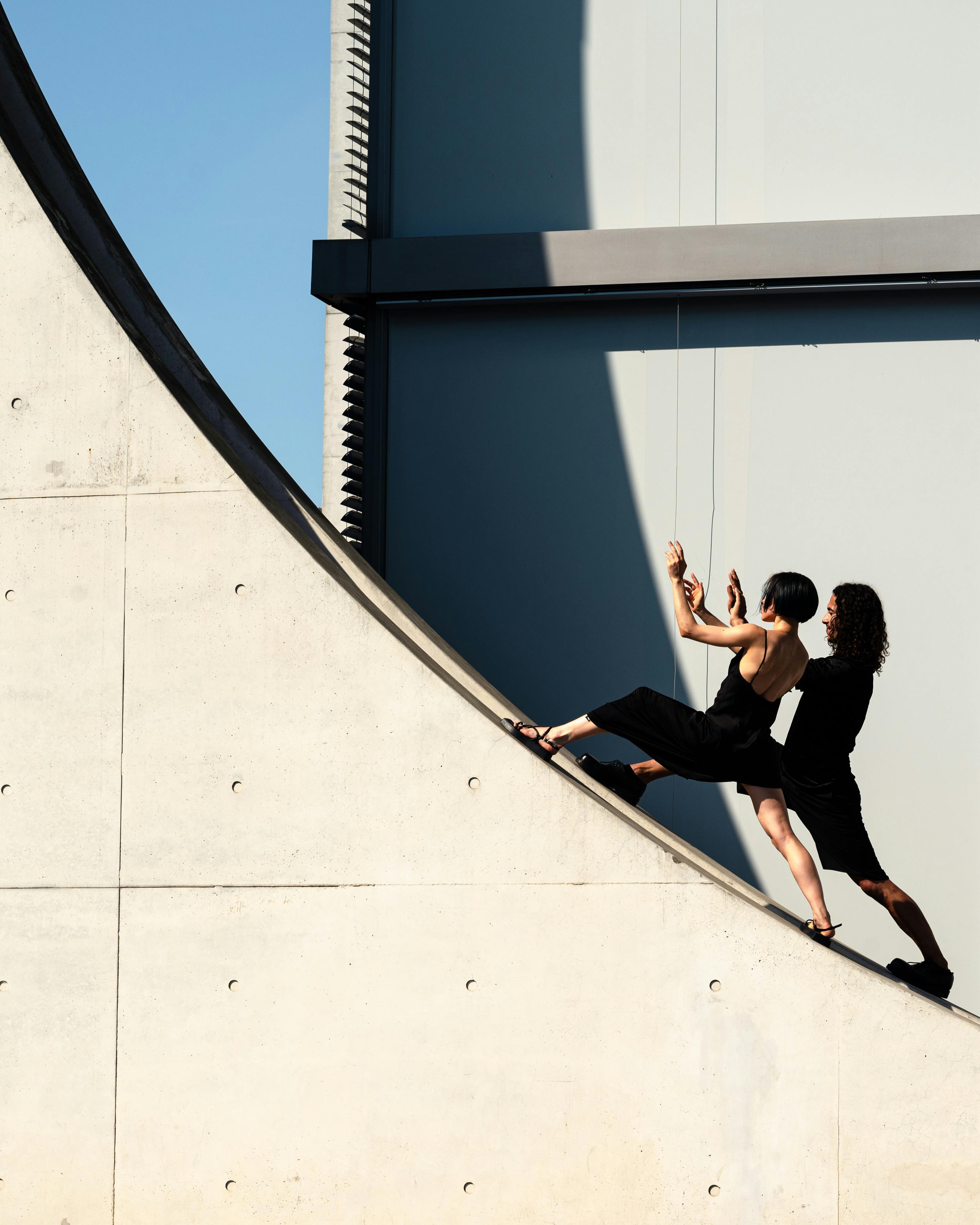 Two women performing a dance pose against modern architecture under clear skies.