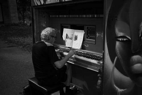 Black and White Photo of a Man Playing Piano on a Street