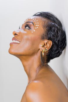 Elegant portrait of a smiling woman looking upwards with artistic face paint and earrings.