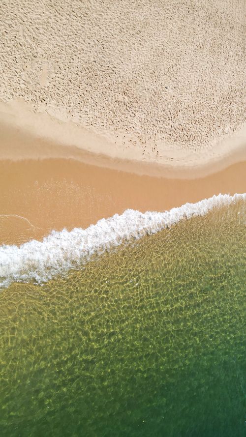 Free Top-down view of waves gently hitting the sandy beach in Rio de Janeiro, Brazil. Stock Photo