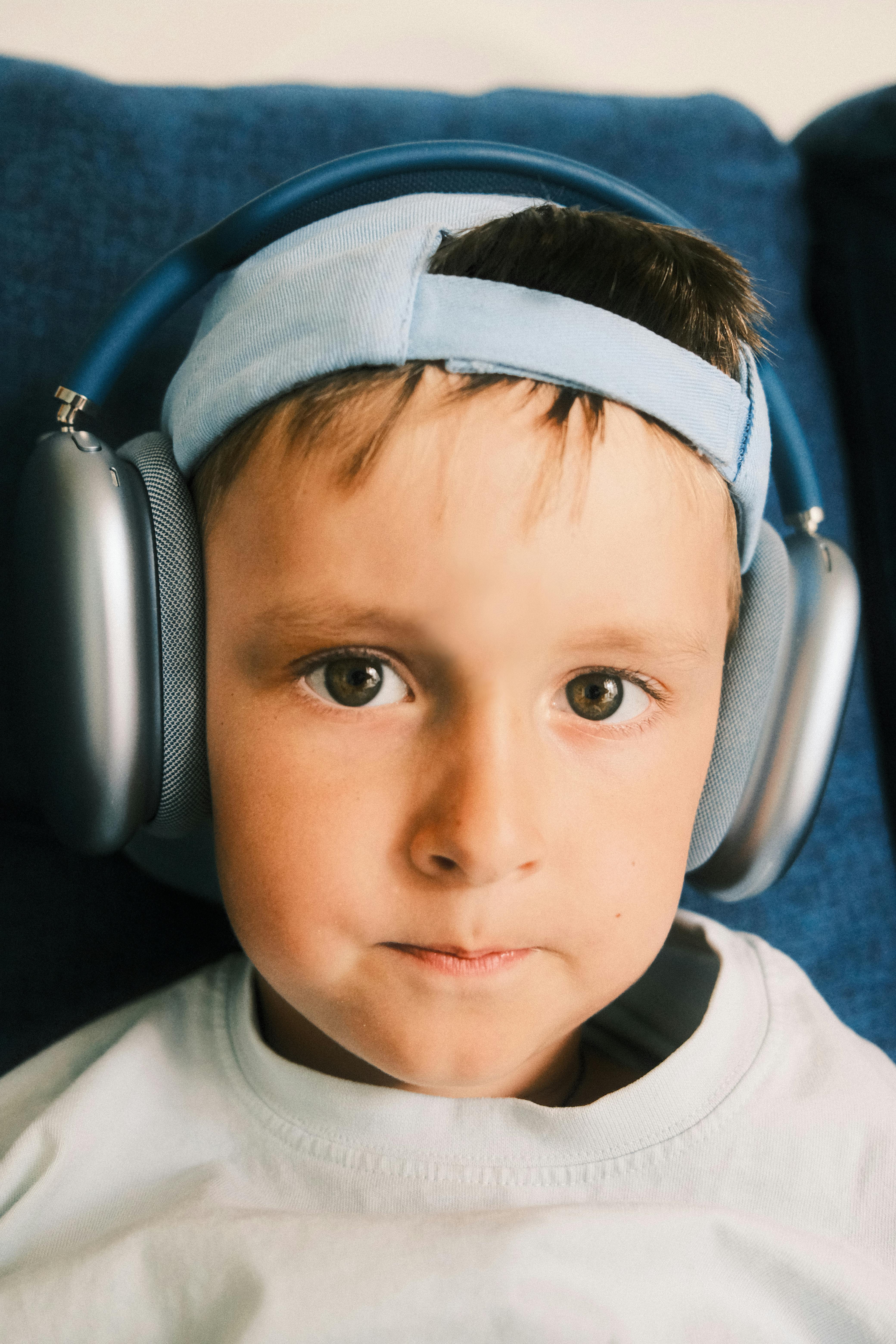 A close-up portrait of a young boy wearing headphones and a cap indoors.