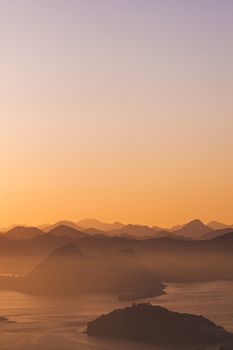 Peaceful sunrise view over a tranquil sea and misty mountains, creating a warm landscape atmosphere.