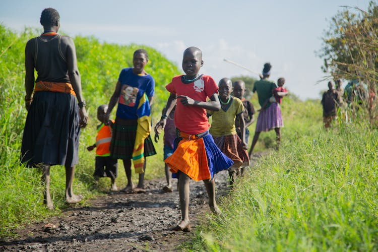 Mothers Watching Over A Group Of Children Running On A Muddy Path