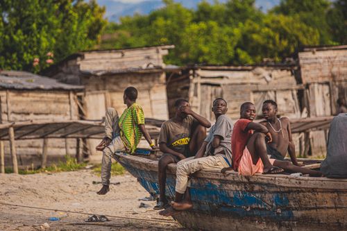 Free Men relaxing on a wooden boat in a rural African village amidst rustic houses. Stock Photo