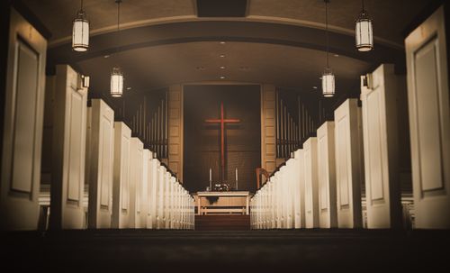 Free A beautiful church interior with a central aisle leading to a cross and altar, illuminated by hanging lights. Stock Photo