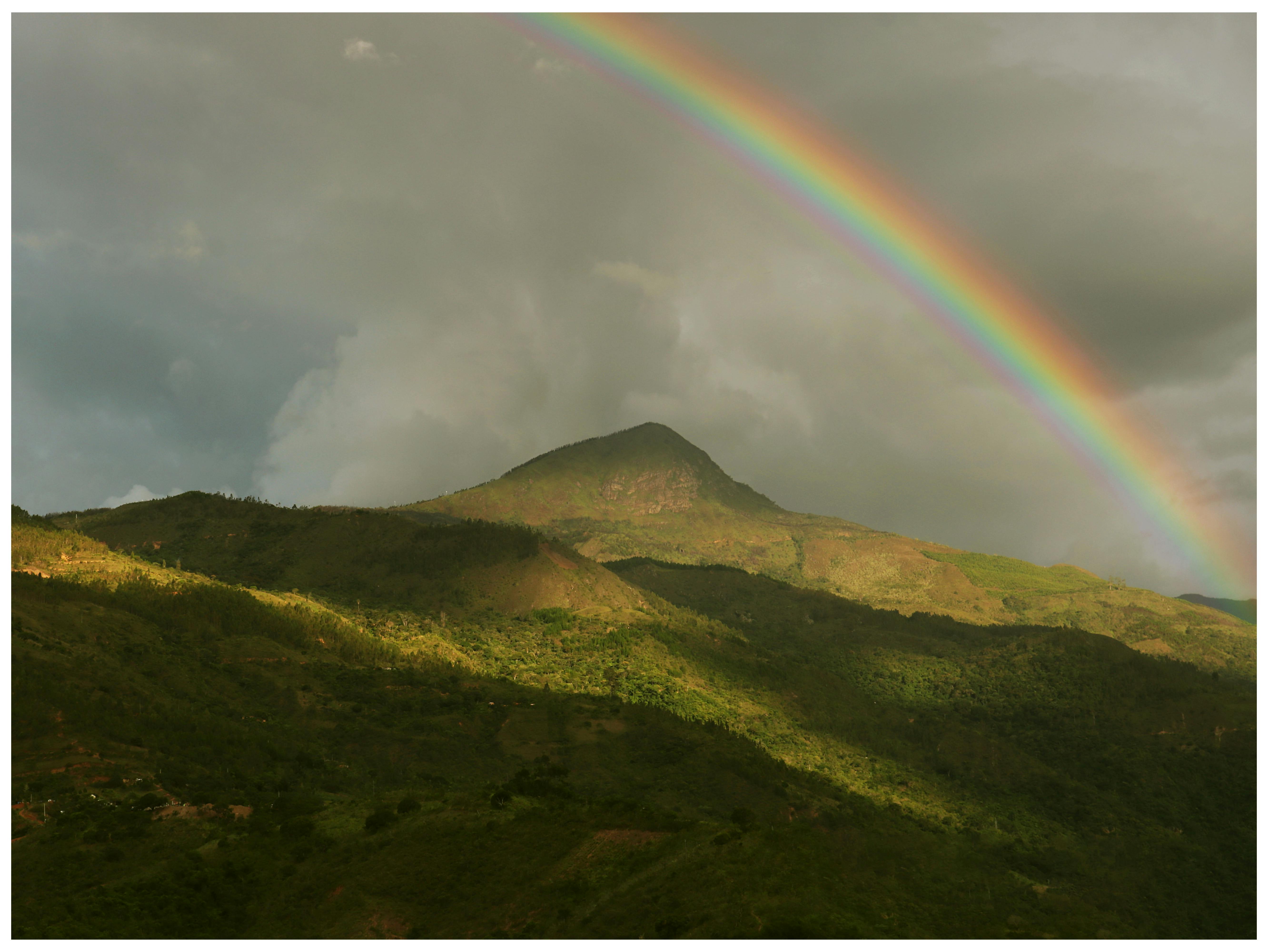A breathtaking view of a mountain landscape under a colorful rainbow on a cloudy day.