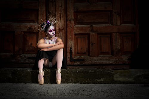 A Girl Dressed as a Catrina Sitting in front of Wooden Door 