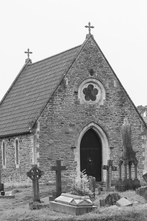 Free Black and white photo of a Gothic stone chapel surrounded by graveyard crosses and tombstones. Stock Photo