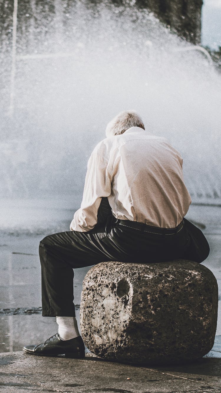 Man Sitting On Rock In Front Of Water Fountain