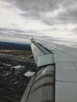 Scenic view from airplane wing over sprawling cityscape under cloudy skies.