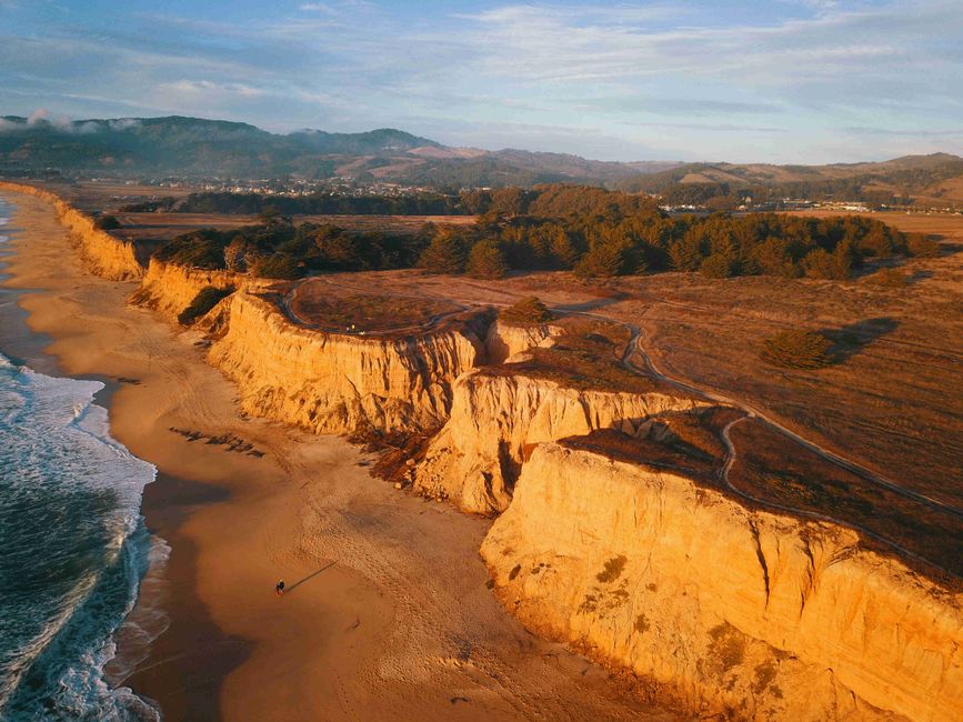 Aerial view of scenic coastal cliffs and ocean waves during sunset with golden hues.